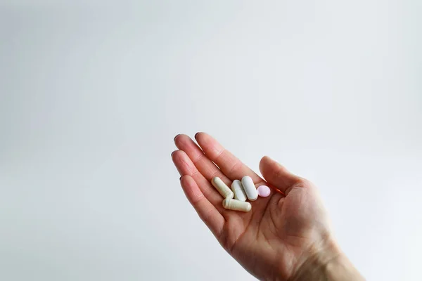 Kız elinde haplar, vitaminler, beyaz bir arka plan üzerinde ilaçlar tutuyor. Beyaz arka planda bir avuç hap ile gerilmiş el
