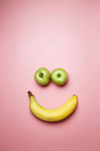 Smiley face with two apples and a banana with copy space on a pink background