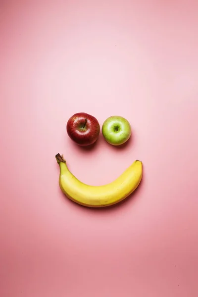 Smiley face with two apples and a banana with copy space on a pink background