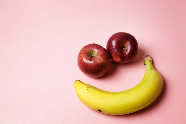 Smiley face with two apples and a banana with copy space on a pink background