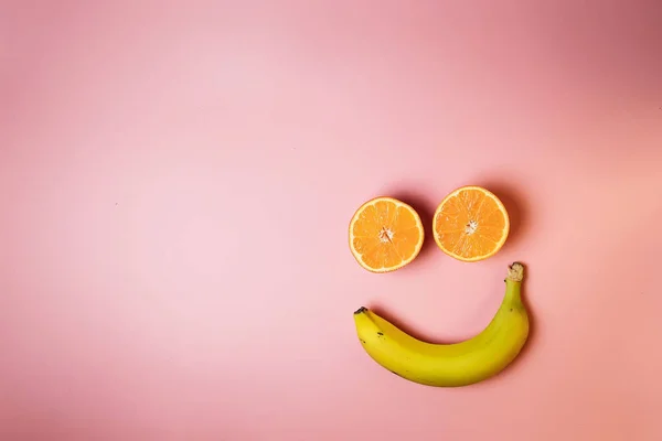 Smiley face with two oranges and a banana with copy space on a pink background