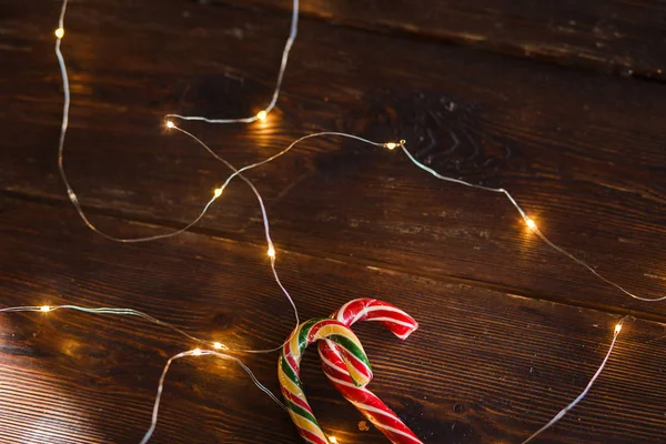 Ahşap arka planda Noel şekerleri ve ışıklar. Noel konsepti, nane çizgili lolipop ve ışıklar bir çelenk, Noel partisi için bir arka plan olarak