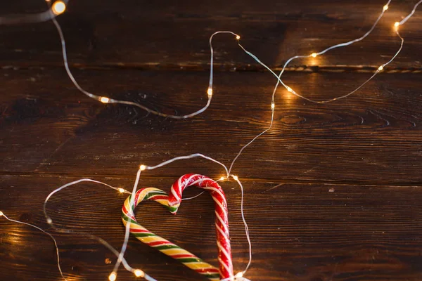 Ahşap arka planda Noel şekerleri ve ışıklar. Noel konsepti, nane çizgili lolipop ve ışıklar bir çelenk, Noel partisi için bir arka plan olarak