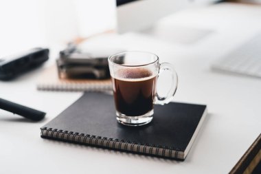 Bilgisayar masasındaki fincanda sade kahve, evdeki masada kahve.