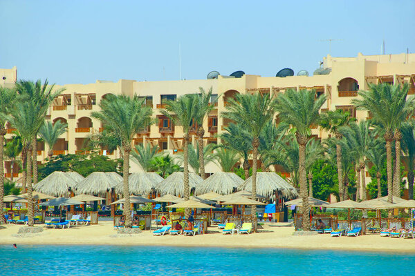 Hurghada / Egypt. 27 July 2018: Tropical resort in Egypt. Palm trees sea sand beach. People rest on beach. People enjoy vacations in seaside resort at Red sea