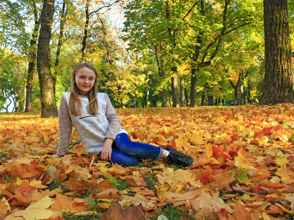 花輪の女の子は 秋の公園で黄色の葉にあります 乾燥した秋に敷設ティーンエイ ジャーの女の子は 都市公園における葉します 秋の散歩 秋の公園散歩します — ストック写真