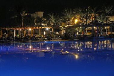 Hurghada Mısır. 28 Temmuz 2018: Mısır Resort Tatil. İnsanlar akşam havuz bir dinlenme var. Işıklar ve akşam Otel palmiye ağaçlarının havuzu suda gecede yansıtılır
