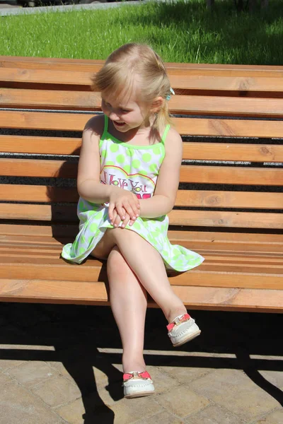 小女孩坐在城市公园的长凳上笑了 积极的孩子们的情绪 心情很好 孩子高兴 快乐的童年 孩子在微笑婴儿尴尬 — 图库照片