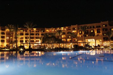 Hurghada Mısır. 28 Temmuz 2018: ışıklar akşam otelin havuzu suda gecede yansıtılır. Hurghada resort Otel'in parlak ışıklar. Kavram seyahat. İnsanlar akşam havuz yakınındaki sakin ol