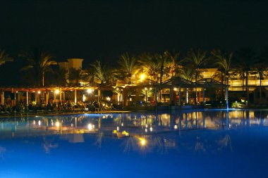 Hurghada / Mısır. 28 Temmuz 2018: havuz ve akşam otel tatil. İnsanlar akşam havuz yakınındaki sakin ol. Işıklar akşam otelin havuzu suda gecede yansıtılır. Hurghada resort Otel'in parlak ışıklar. İnsanlar relax havuz