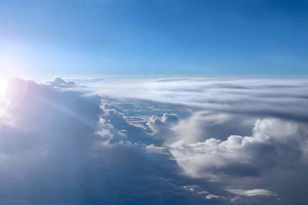 Wonderful view from window of plane in morning sun over clouds. Unusual clouds illuminated by rays of sun. Beautiful white clouds on blue sky background. Landscape with sun and sky. Heaven panorama