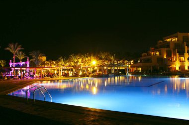 Hurghada/Mısır. 31 Temmuz 2018: havuz ve akşam otel tatil. İnsanlar akşam havuz yakınındaki sakin ol. Işıklar akşam otelin havuzu suda gecede yansıtılır. Hurghada resort Otel'in parlak ışıklar. İnsanlar relax havuz