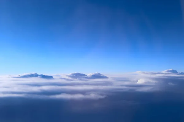 view from window of plane to white clouds. Unusual clouds illuminated by rays of sun. Beautiful white clouds on blue sky background. Landscape with sun and sky. Heaven panorama