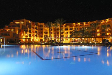 Hurghada/Mısır. 31 Temmuz 2018: havuz ve akşam otel tatil. İnsanlar akşam havuz yakınındaki sakin ol. Işıklar akşam otelin havuzu suda gecede yansıtılır. Hurghada resort Otel'in parlak ışıklar. İnsanlar relax havuz