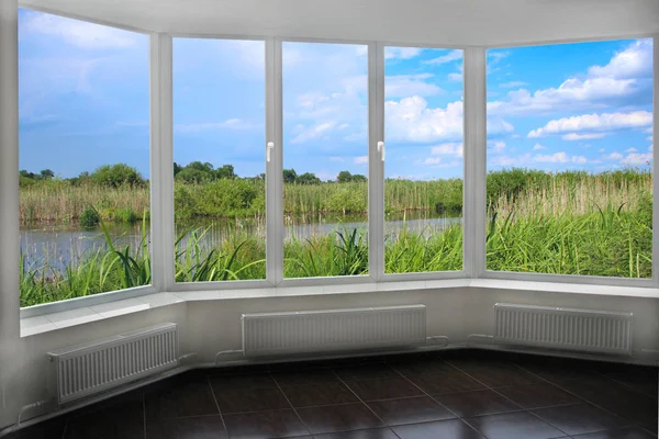 Room with wide window overlooking landscape with lake surrounded with cane. View from room window to brushwood of rush in lake. Beautiful natural landscape with pond from window
