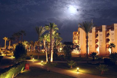 Hurghada / Mısır. 27 Temmuz 2018: tropikal resort otel binası ve palmiye ağaçları ile geceleri aydınlatıcı ay ışığı. Gece resort güzel çim footpathes ve palmiye ağaçları arasında çim ile