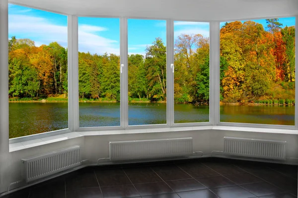 Room with window with view to autumn forest and lake. Autumnal landscape with lake in forest. Panoramic view to nature from room window. View from window to colored autumn trees