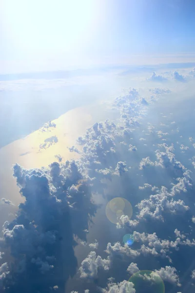 Beautiful view from window of plane flying over clouds and sea surface. Natural panorama with clouds. White clouds moving above water surface of sea. Landscape with sun reflected in sea surface