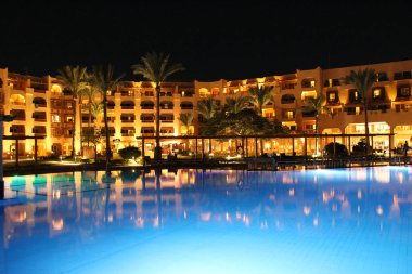 Hurghada/Mısır. 31 Temmuz 2018: havuz ve akşam otel tatil. İnsanlar akşam havuz yakınındaki sakin ol. Işıklar akşam otelin havuzu suda gecede yansıtılır. Hurghada resort Otel'in parlak ışıklar. İnsanlar relax havuz