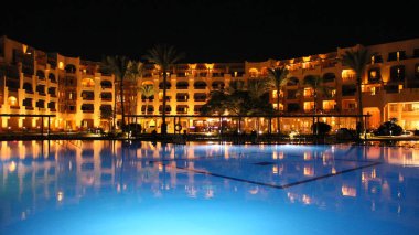Hurghada/Mısır. 31 Temmuz 2018: havuz ve akşam otel tatil. İnsanlar akşam havuz yakınındaki sakin ol. Işıklar akşam otelin havuzu suda gecede yansıtılır. Hurghada resort Otel'in parlak ışıklar. İnsanlar relax havuz