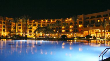 Hurghada / Mısır. 28 Temmuz 2018: Yüzme Havuzu ve akşam otel tatil günlerinde. İnsanlar akşam havuz yakınındaki rahatlayın. Işıklar akşam otelin havuzu suda gecede yansıtılır. Hurghada resort Otel'in parlak ışıklar. İnsanlar relax havuz