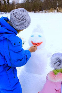 Anne ve kızı kardan adam boya. Kardan adam yüzünü kapat. Kış tatil zevk. Yeni yıl özniteliği. Kış aile tatil. Yeni yıl kardan adam gülümse çizim kadın