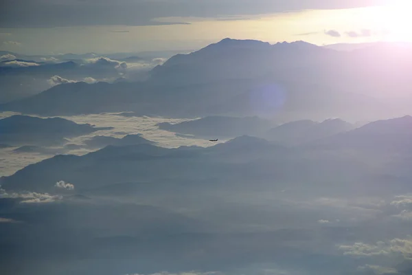 Beautiful view from window of plane. View from plane window to another plane flying over clouds and mountains in sunny rays. Panorama with flying plane high in sky above mountain ridge and clouds