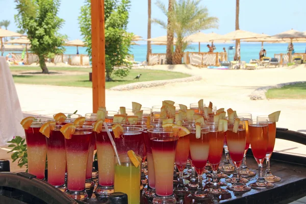 Bright cocktails in background of tropical resort with palm trees, sea and people. Holiday concept. Drink in vacations. Summer holiday