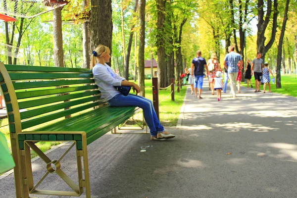 Young woman sitting on bench in beautiful park with many green trees — Stock Photo, Image