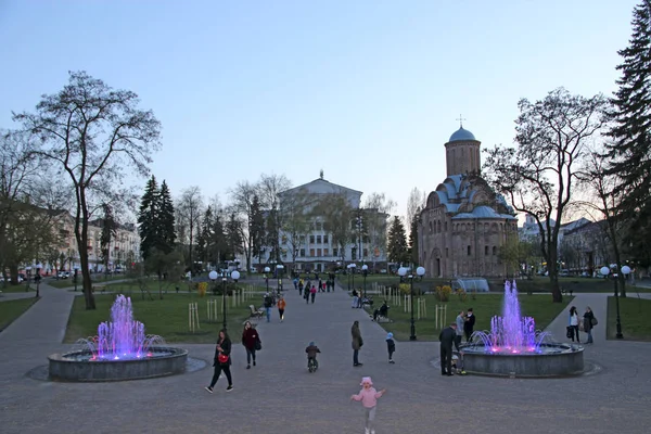 Stadtpark mit Menschen, die zwischen Springbrunnen mit farbigem Wasser spazieren — Stockfoto