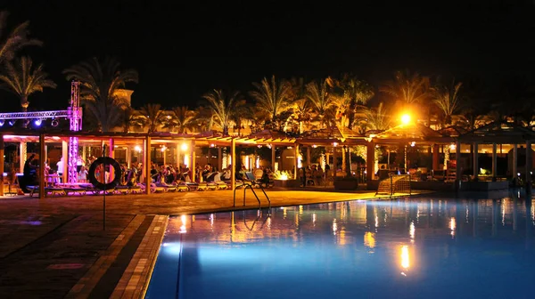 Swimming pool and night hotel on holidays. People relax in evening near pool — Stock Photo, Image