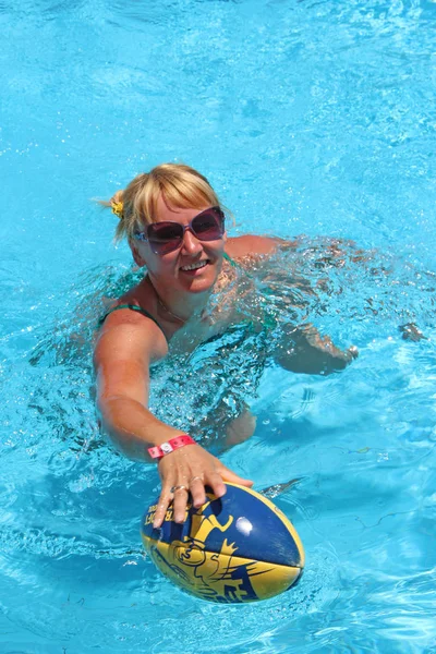 Fashionable woman with ball for rugby swimming in blue water of pool