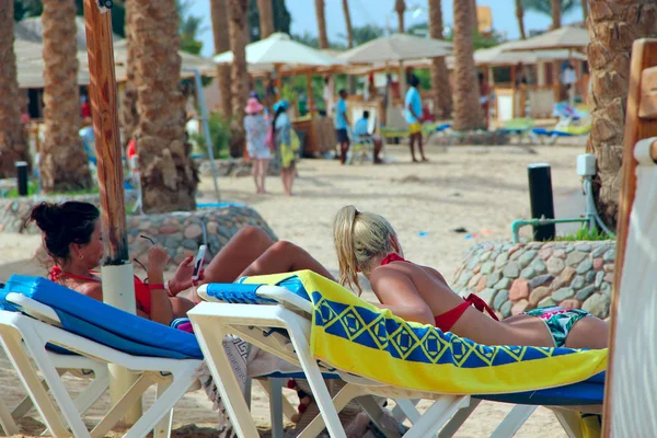 Las mujeres turistas yacen en chaise longues mientras se relajan en el resort tropical — Foto de Stock