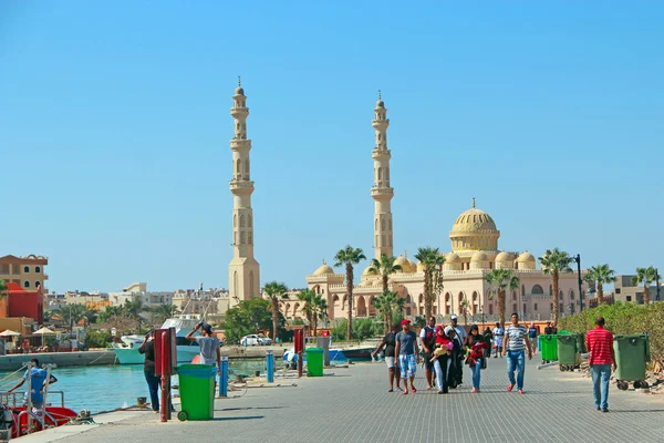 Turistas árabes caminan a lo largo de terraplén contra telón de fondo de la mezquita en Hurghada —  Fotos de Stock