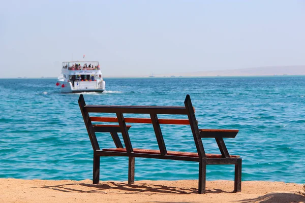 Banco vacío cerca del mar y barco embarcado. Turismo de masas en el mar. Banco cerca de la playa — Foto de Stock