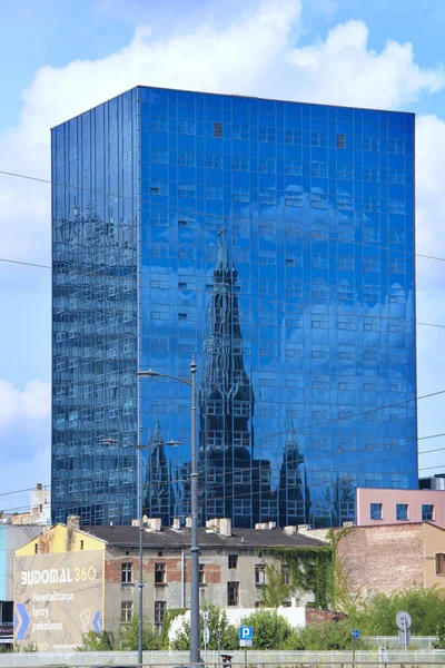 Lång skyskrapa med kyrklig reflektion i fönster i Lodz. — Stockfoto