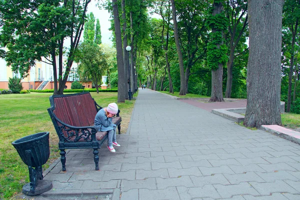 little girl with thoughtful look sitting on bench in city park and thinking