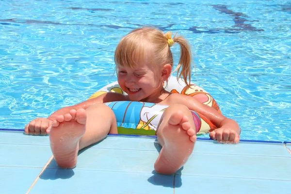 Niña sonriente con bonitas trenzas nadando en la piscina acostada en un círculo inflable Fotos de stock