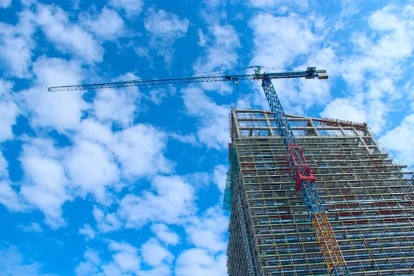 建設クレーン複数階建ての建物の建設中に負荷を持ち上げる 青い空に対する超高層ビルの建設 集合住宅 近代建築 フラットのスタイリッシュな生活ブロック — ストック写真