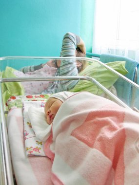 Yeni doğan bebek hastanede ve genç anne. Yeni doğmuş bebek doğum hastanesinde uyuyor. Mutlu anne telefonda konuşuyor ve yeni doğmuş bebeği tebrik ediyor.