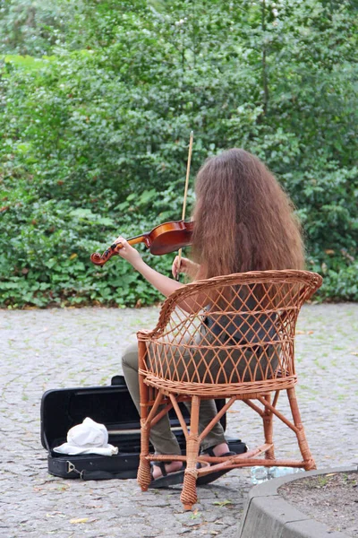 路上でバイオリンを弾いている少女です バイオリンを弾いている女の子に背部からの眺め ストリートミュージシャン 路上で音楽 夏の公園で音楽 女の子は公園でバイオリンを弾くことで生計を立てています — ストック写真