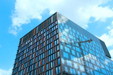 Lodz / Polonya. 22 Temmuz 2019: İnşaat vinci çok katlı binanın inşaatı sırasında binanın camlarına yansıyor. Gökdelenin inşaatı. Apartman binası. Modern mimari. Kaliteli apartman blokları