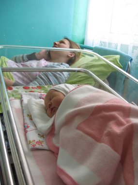 Yeni doğan bebek hastanede ve genç anne. Yeni doğmuş bebek doğum hastanesinde uyuyor. Mutlu anne telefonda konuşuyor ve yeni doğmuş bebeği tebrik ediyor.