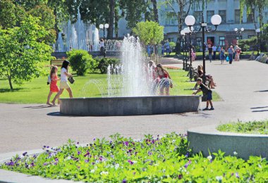 Chernihiv - Ukrayna. 27 Ağustos 2016: Şehir çeşmelerinde suya yaya olarak dokunmaya çalışan küçük bir kız. İnsanlar şehir parkında fıskiyeli dinleniyor. Güneşli bir yaz günü. Çocuk şehir çeşmesinin suyuyla oynuyor. Yaşam tarzı kavramı