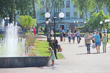 Chernihiv - Ukrayna. 27 Ağustos 2016: Şehir çeşmelerinde suya yaya olarak dokunmaya çalışan küçük bir kız. İnsanlar şehir parkında fıskiyeli dinleniyor. Güneşli bir yaz günü. Çocuk şehir çeşmesinin suyuyla oynuyor. Yaşam tarzı kavramı