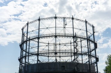 Gasometer eski endüstri mirası ile bulutlu gökyüzü ve yaz ağacında