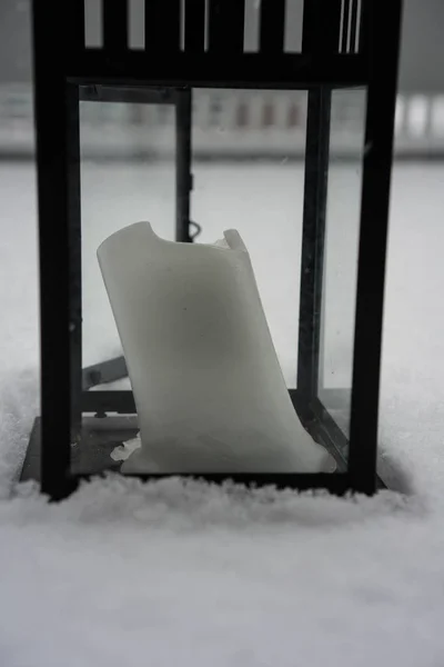 Witte kaars in zwarte lantaarn staande in de sneeuw — Stockfoto