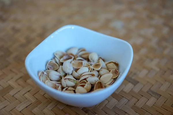 Орехи фисташки в белой керамической миске и деревянный фон — стоковое фото