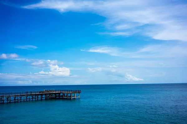 Molo di legno e acque calme dell'oceano con cielo blu e nuvole — Foto Stock
