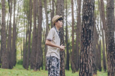 Asya adam gömlek, şapka ve kamuflaj pantolon giyiyor ormanda yürüyüş ve fotoğraf çekmek.